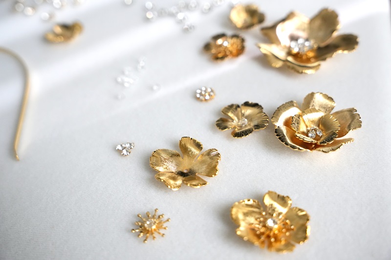 Close-up image of gold-colored floral metal decorations and small silver beads scattered on a white surface.